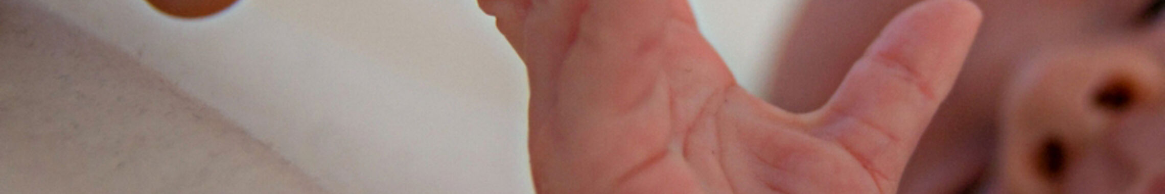 Ein Neugeborenes wird sanft an den Fingern berührt.