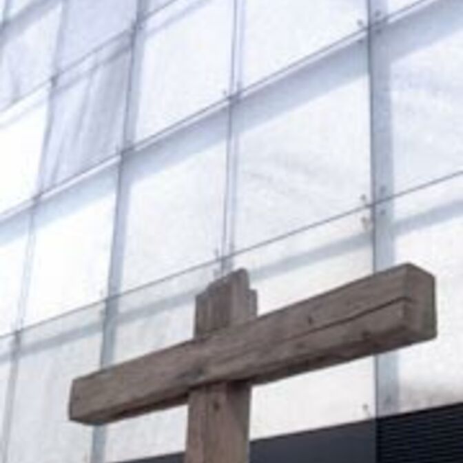 Ein Holzkreuz vor der Glasfassade eines Firmengebäudes.